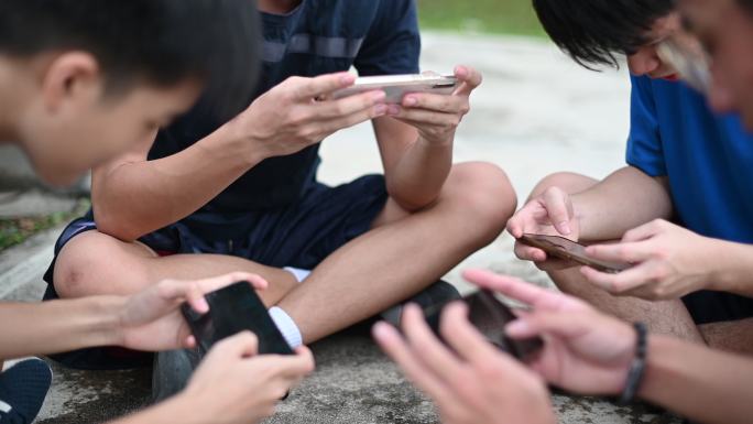 少年放学后用手机在篮球场上玩手机游戏