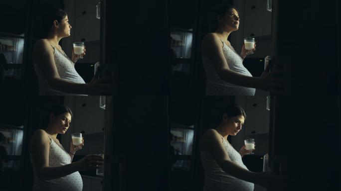 怀孕的年轻女子站在冰箱前喝着一杯牛奶