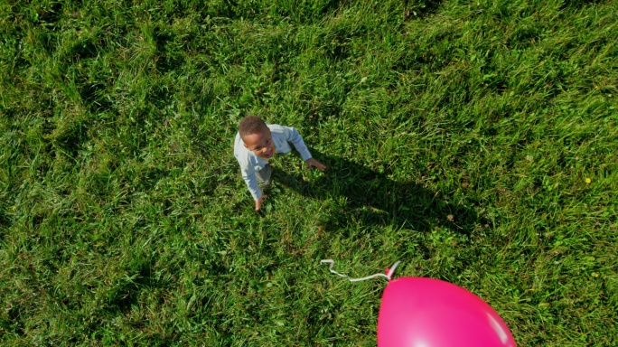 小男孩在阳光明媚的草地上释放粉色气球