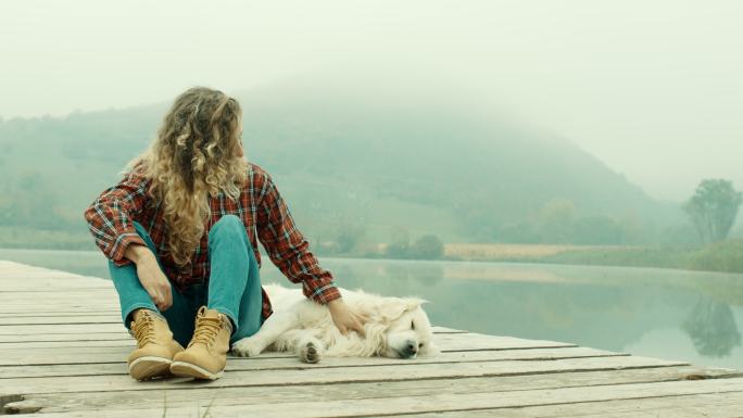年轻女子和狗一起在湖边的码头