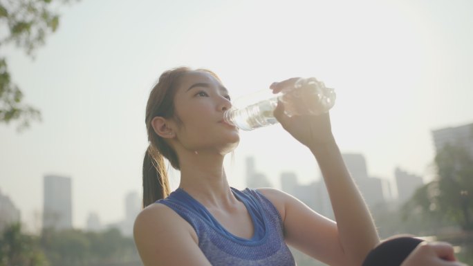 女子一边在户外运动一边对着夕阳喝水