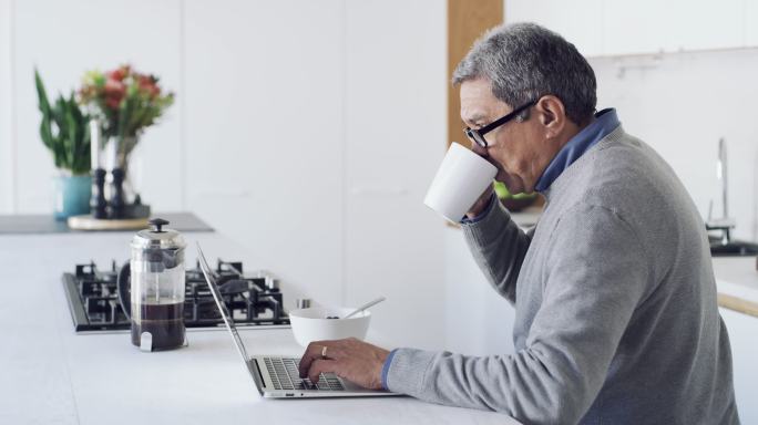 一名老人在家吃早餐时使用笔记本电脑