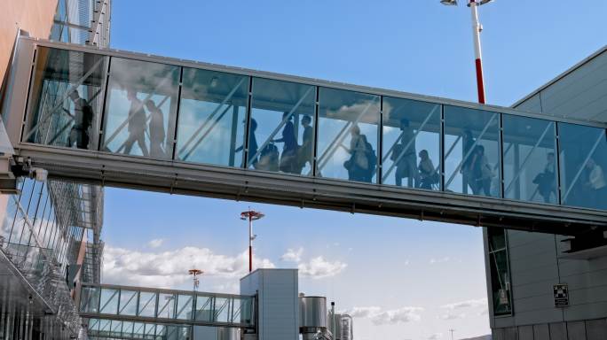 乘客穿过玻璃登机桥下飞机