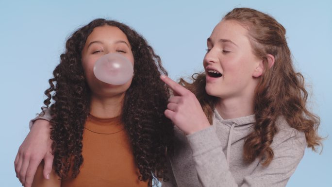 两名少女在蓝色工作室背景下嚼口香糖吹泡泡