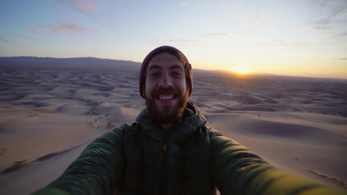 日落时在戈壁沙漠沙丘上的男子自拍