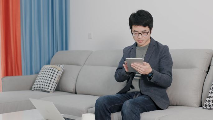 4K年轻男性在家坐沙发上用平板电脑办公