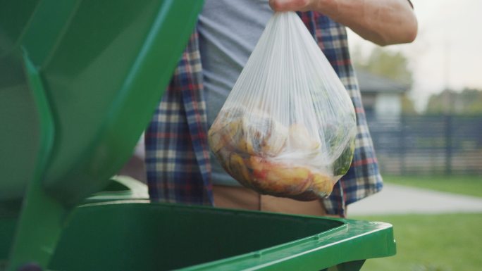 男性将生物食物垃圾扔进绿色垃圾桶