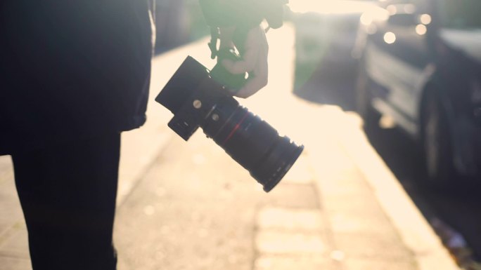 专业摄影记者拿着相机，走在街上，狗仔队在监视