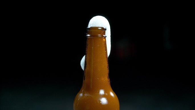 一个啤酒瓶在黑色工作室背景下冒出泡沫