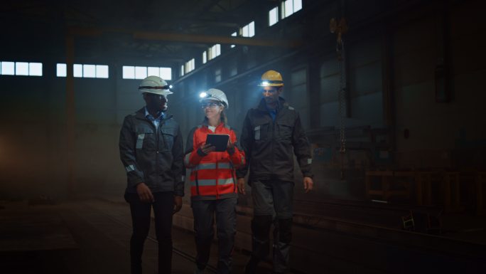 三重工业工程师在黑暗的钢铁厂里行走。