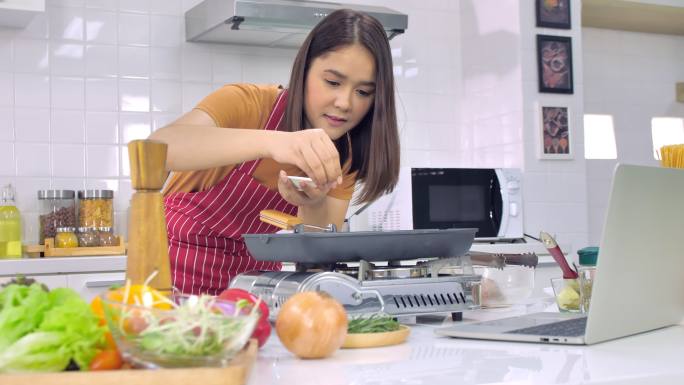 年轻的女人在家里的厨房里做饭。