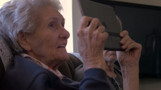 一位90多岁的老妇人看着一台数码平板电脑，笑着