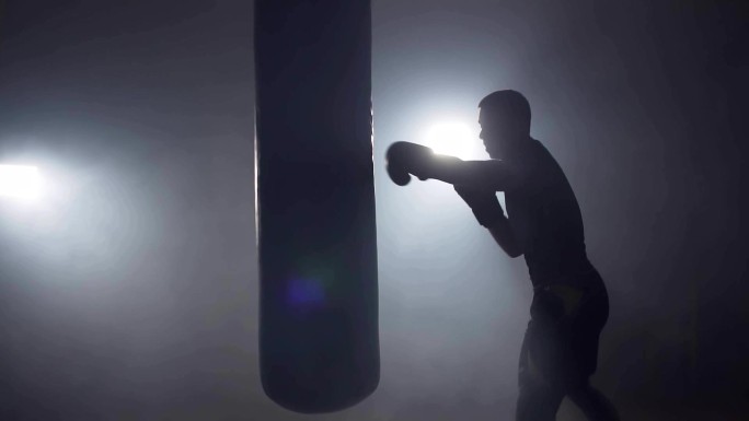 拳击手在黑暗的健身房里打拳击袋。