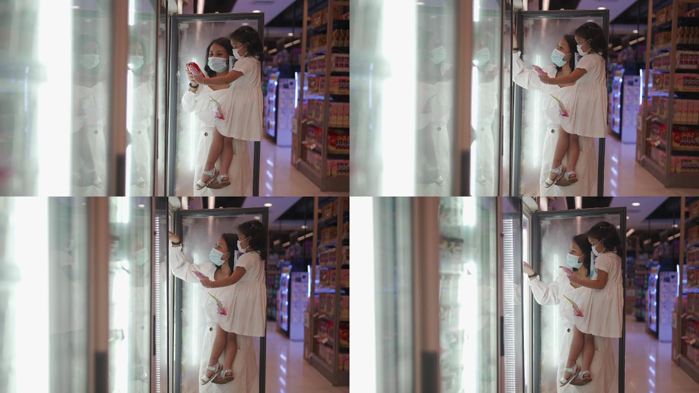 妈妈抱着小女儿在超市冰箱的货架上挑选食物
