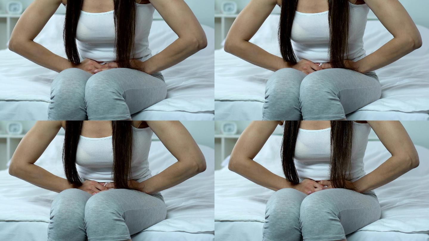 女性抱着肚子坐在床上，月经来潮，腹痛，疾病