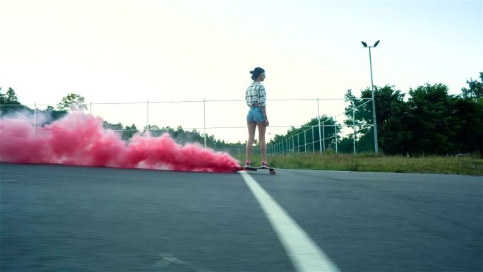 女孩在城市道路上骑着冒着红烟的木制滑板