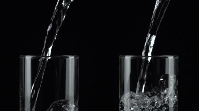 垂直和慢动作：将水倒进黑色背景上的一个玻璃杯中。
