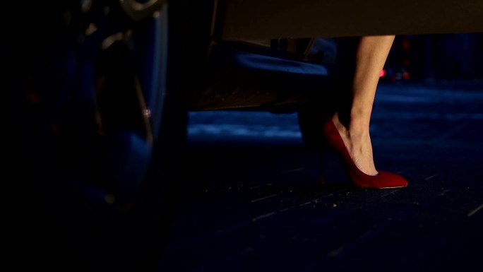 穿着红色高跟鞋的女人晚上从车里走出来