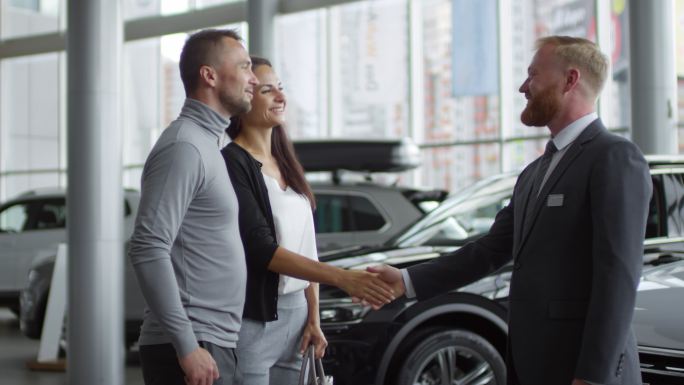 一对幸福的夫妇在汽车展厅与销售员握手