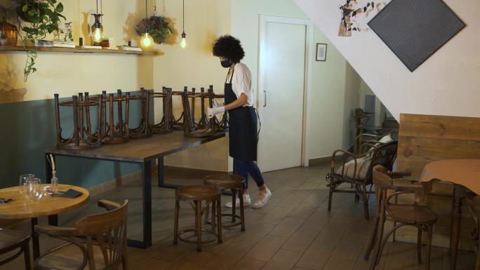 年轻的女店主在咖啡店里摆好桌椅。