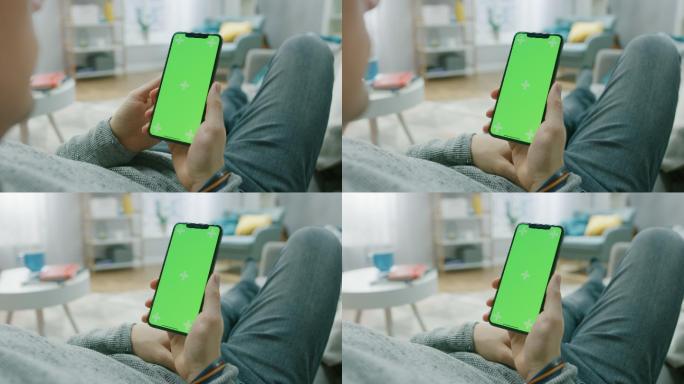 家中的男人躺在沙发上，用带有绿色模拟屏幕的智能手机