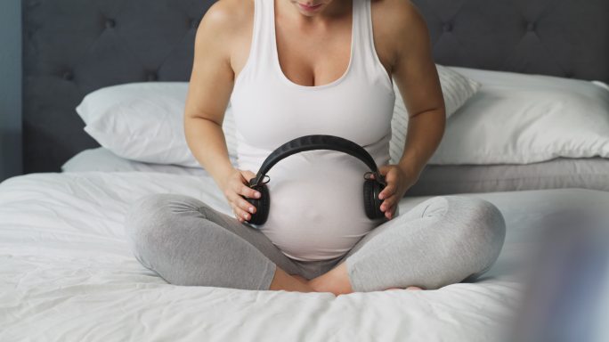 一名年轻女子在怀孕的肚子上戴着耳机