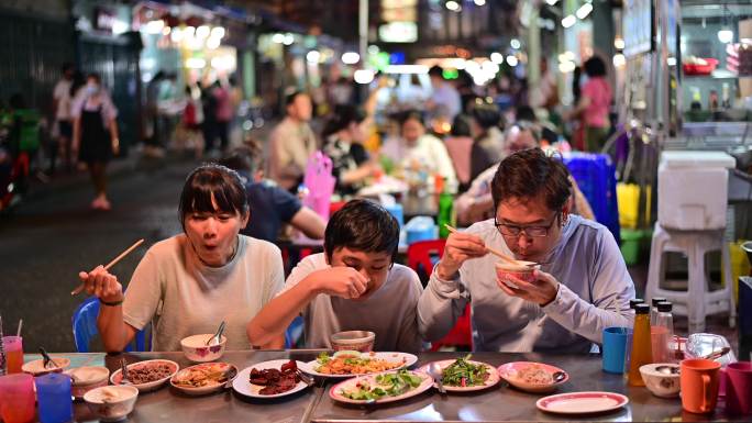 一家三口和一群人一起在街上的美食餐厅吃饭