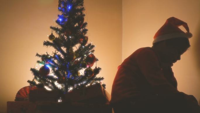 坐在圣诞树旁的悲伤的小男孩