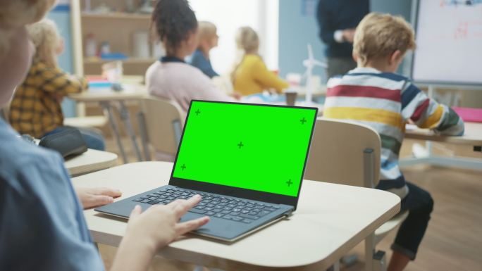 一个孩子在课堂上使用绿色模拟屏幕电脑