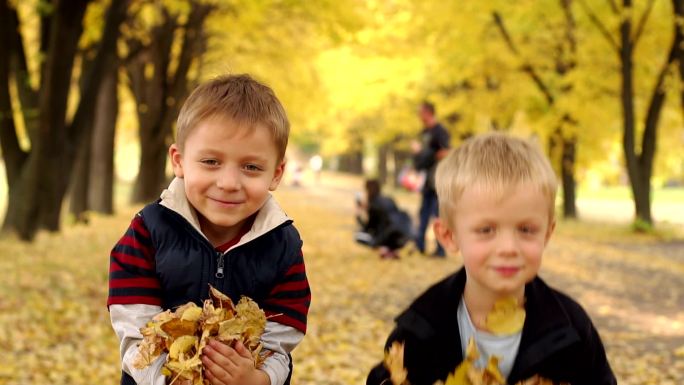 两个快乐的小男孩在秋天的公园里扔黄叶