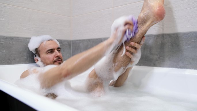 男子躺在浴缸里用泡沫和海绵清洗身体
