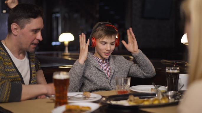 儿子戴上耳机，父母在餐厅里责骂男孩