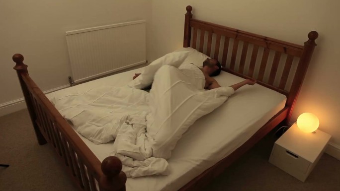 一个年轻人夜晚在床上翻来覆去的画面。