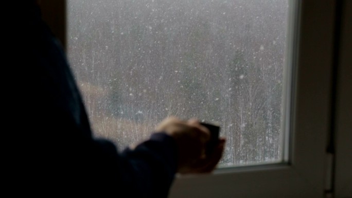 在窗边喝茶的男人冬季寒冷室内取暖飘雪雪花