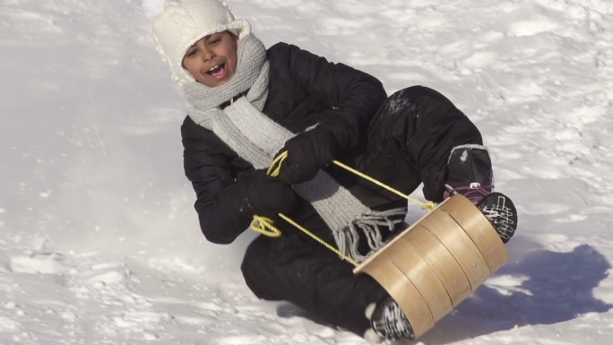 小男孩的雪橇在雪坡上滑行