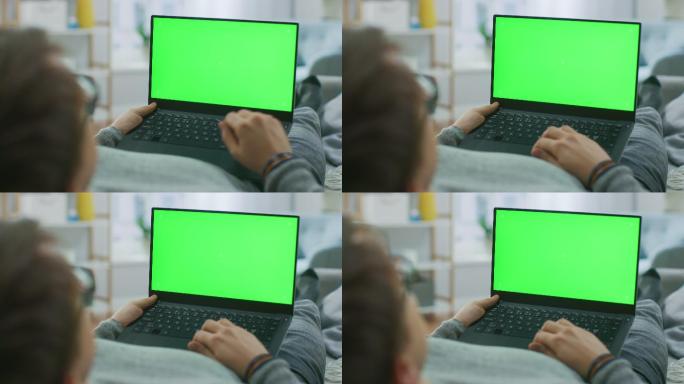 一名男子躺在沙发上，用绿屏笔记本电脑