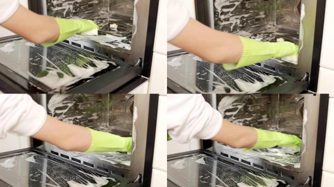 使用防护手套清洁烤箱的女性手的特写