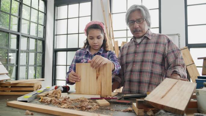 小女孩和爷爷在家的木棚里学习木工。