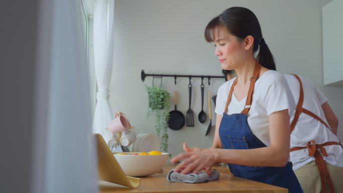 年轻夫妇穿着围裙，在家里打扫厨房。