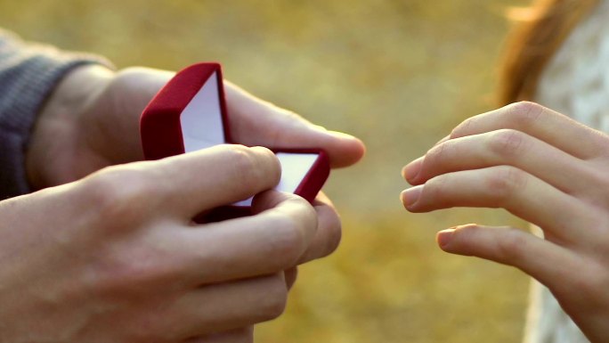 男子将银订婚戒指戴在女子手上，在秋季公园求婚