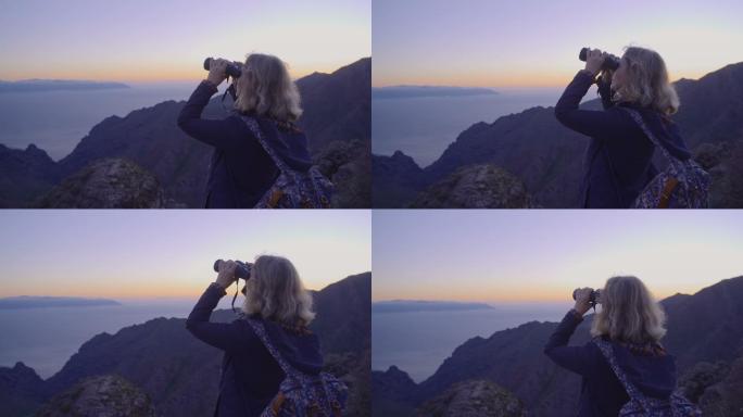 在山顶徒步旅行的女性用双筒望远镜看风景