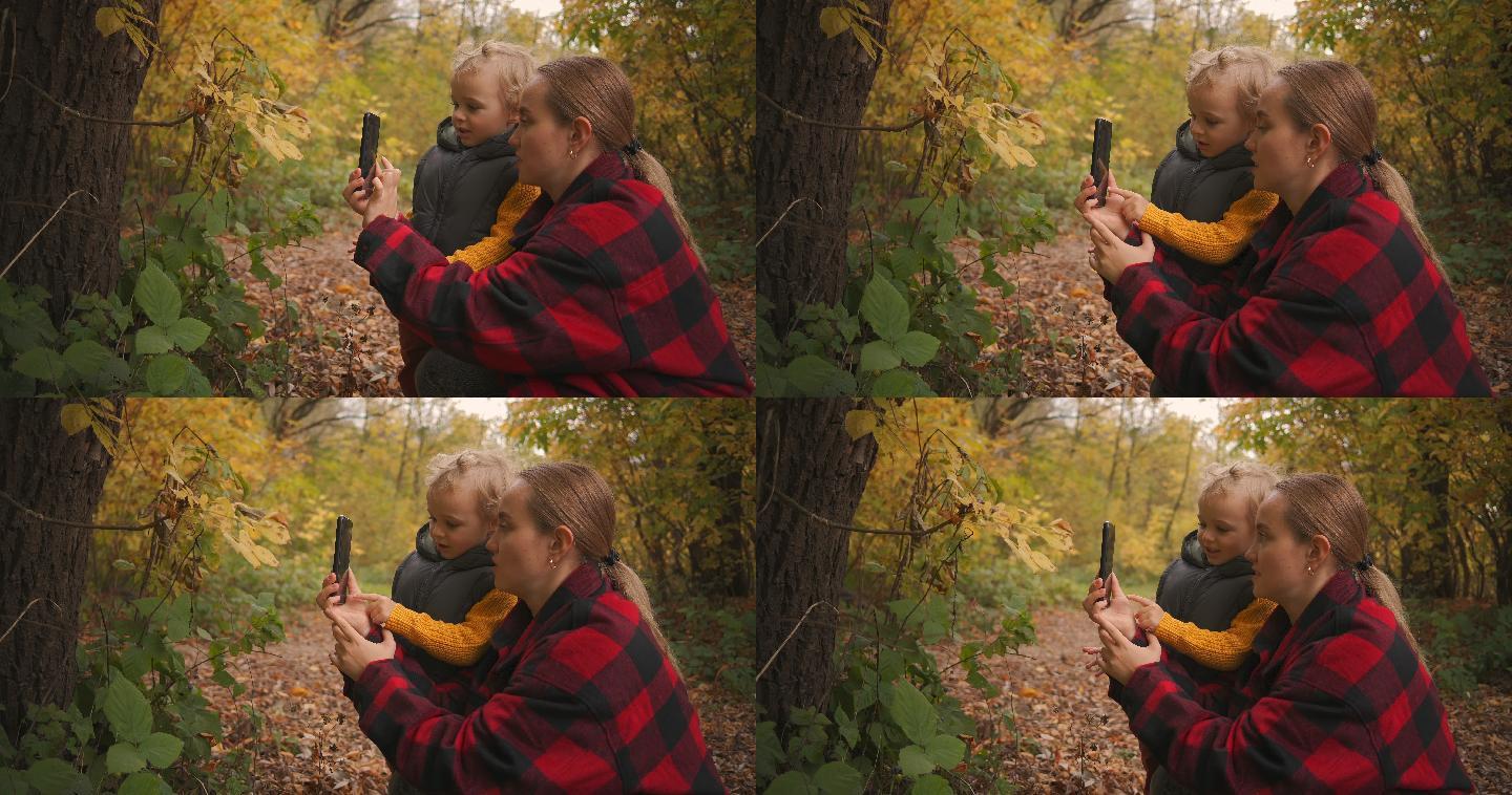 母亲在教他的小儿子在森林里用手机拍照