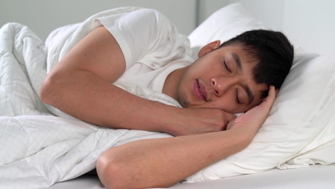 年轻人早上睡在舒适的床上。