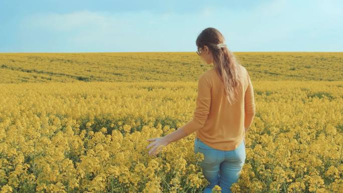女人走在田野里轻轻抚摸盛开的黄色油菜花
