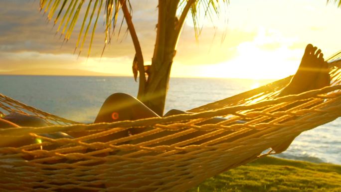 日落时分，一对浪漫的情侣在热带吊床上放松