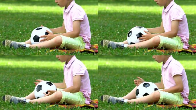 孤独的男孩带着球坐在公园里