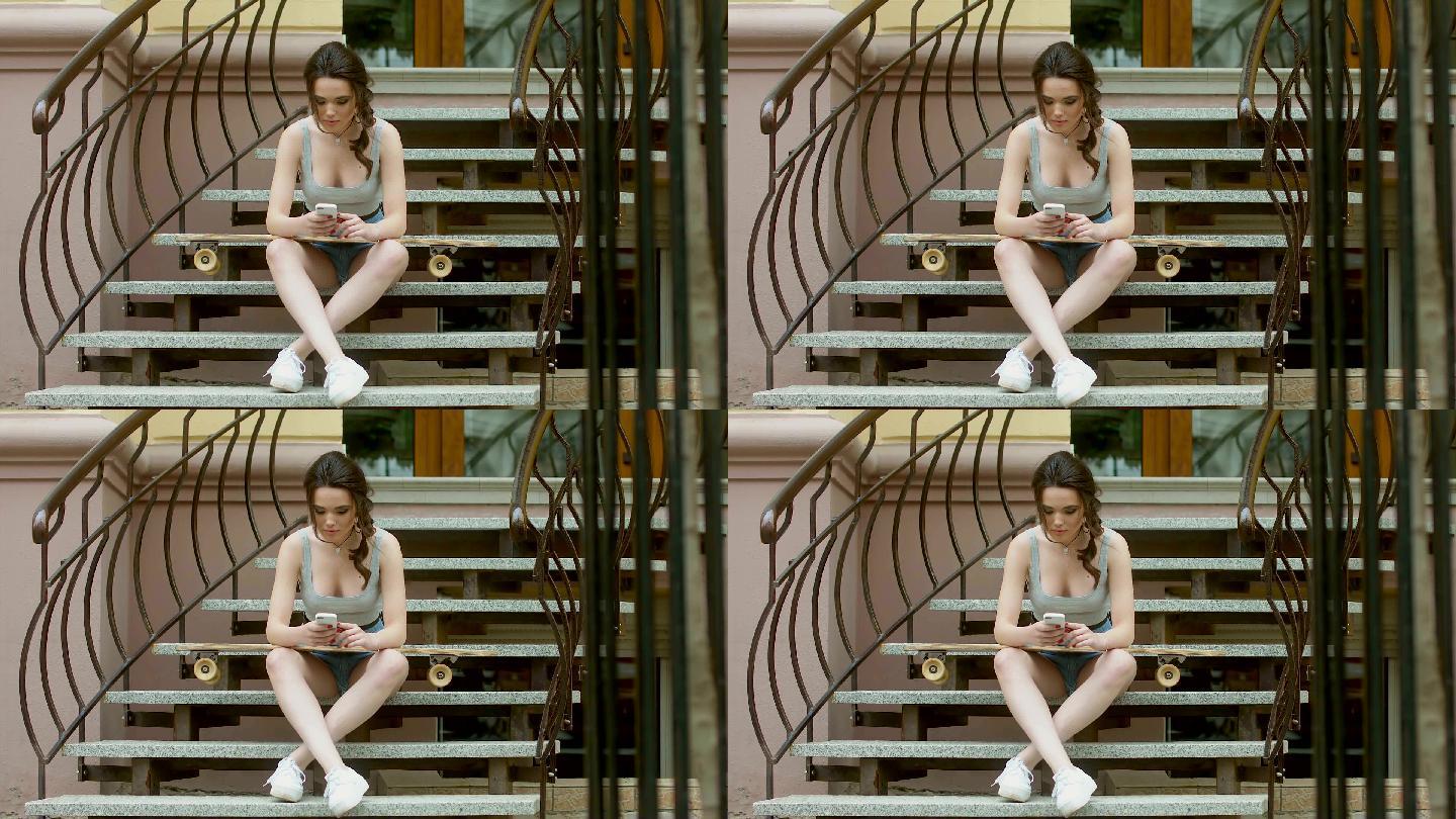 女孩坐在楼梯上，拿着长板滑板，使用手机