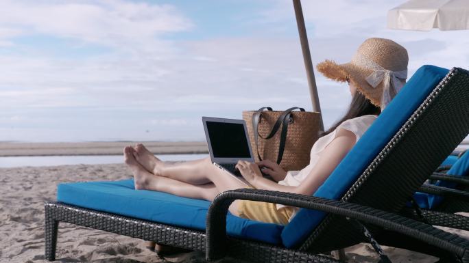 在海滩沙滩椅上使用笔记本电脑的一名妇女