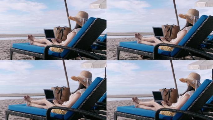 在海滩沙滩椅上使用笔记本电脑的一名妇女