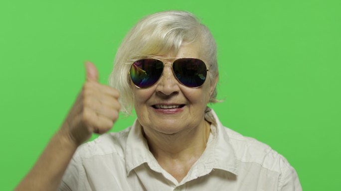 一位戴太阳镜的老妇人竖起大拇指微笑着。